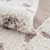 Close-up of the Zhen Pink Spots Leopard Rug showing the shag texture and pink and brown spots on an off-white background. Fold