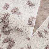 Close-up of the Zhen Pink Spots Leopard Rug, showing its shag texture, off-white base, and pink and brown leopard spots. Fold