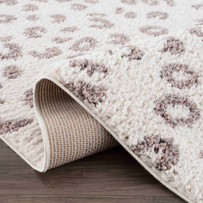 Close-up of the Zhen Pink Spots Leopard Rug, a shag rug with off-white and pink leopard spots on a wood floor. Fold