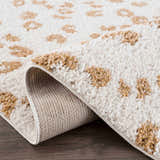 Close-up of the Altin Area Rug. White shag rug with a yellow animal print pattern. Machine woven polyester rug. Fold