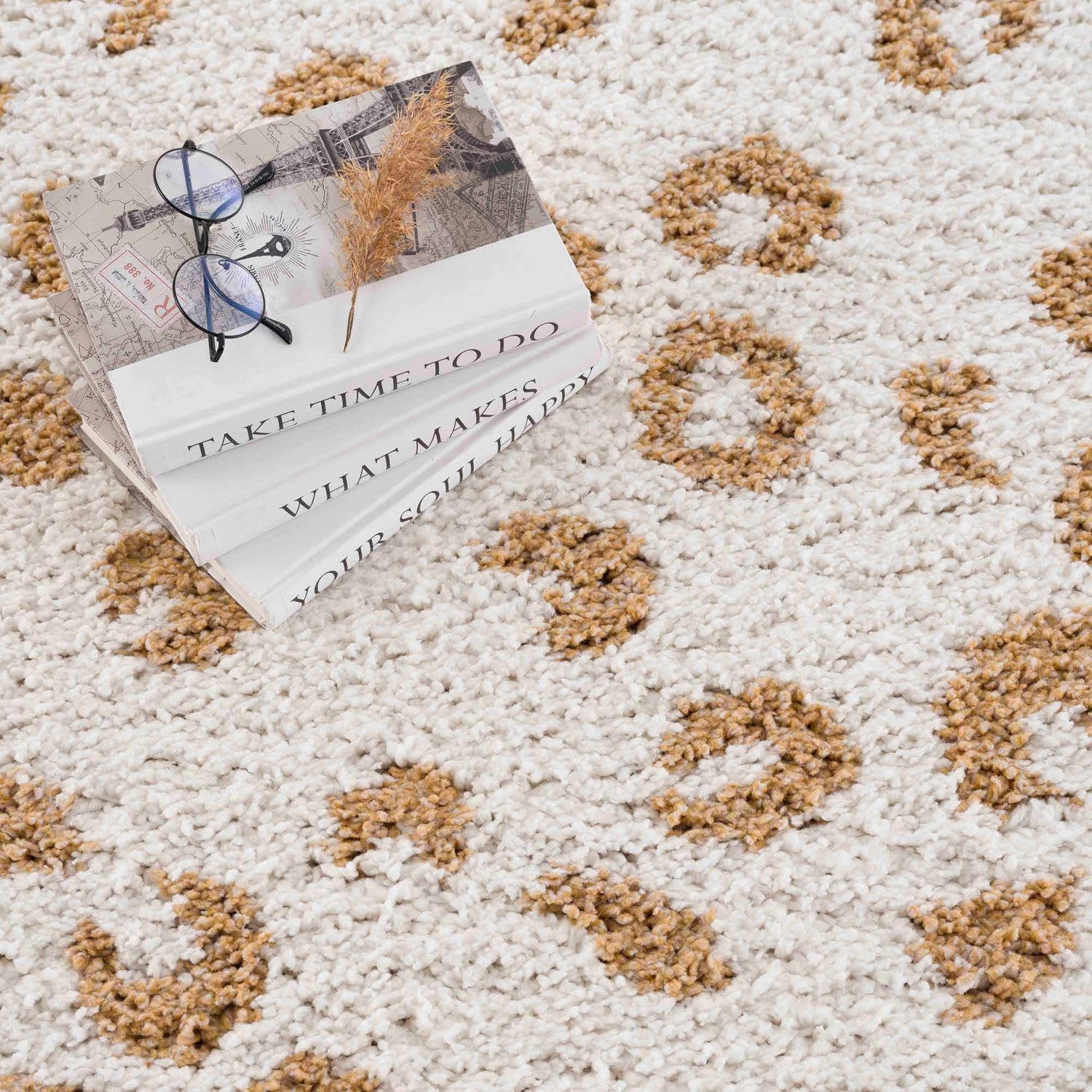 Close-up of the Altin Area Rug, a white shag rug with a yellow animal print pattern. Books and glasses are styled on the rug. Styleshot