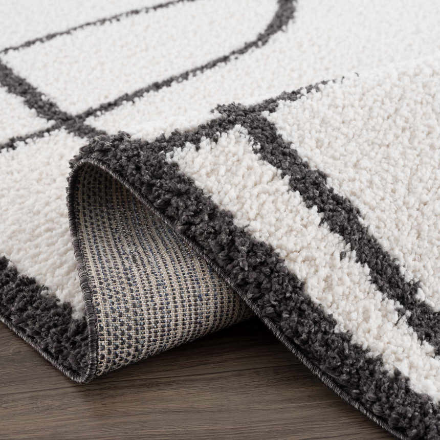 Close-up of the Brad Area Rug showing its black geometric pattern on a white shag pile, and the rug's backing. Fold