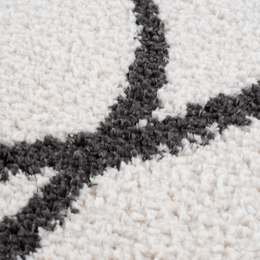 Close-up of the Brad Area Rug showing its shag texture and black geometric design on a white background. Texture