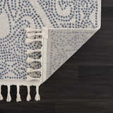 Close-up of Birdwood Navy Area Rug showing cream and blue pattern, tassels, and rug backing on dark wood floor. Fold
