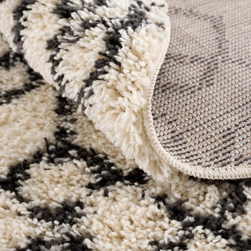 Close-up of the Muni Berber Shag Rug, showing its charcoal and light beige colors, shag texture, and woven backing. Fold