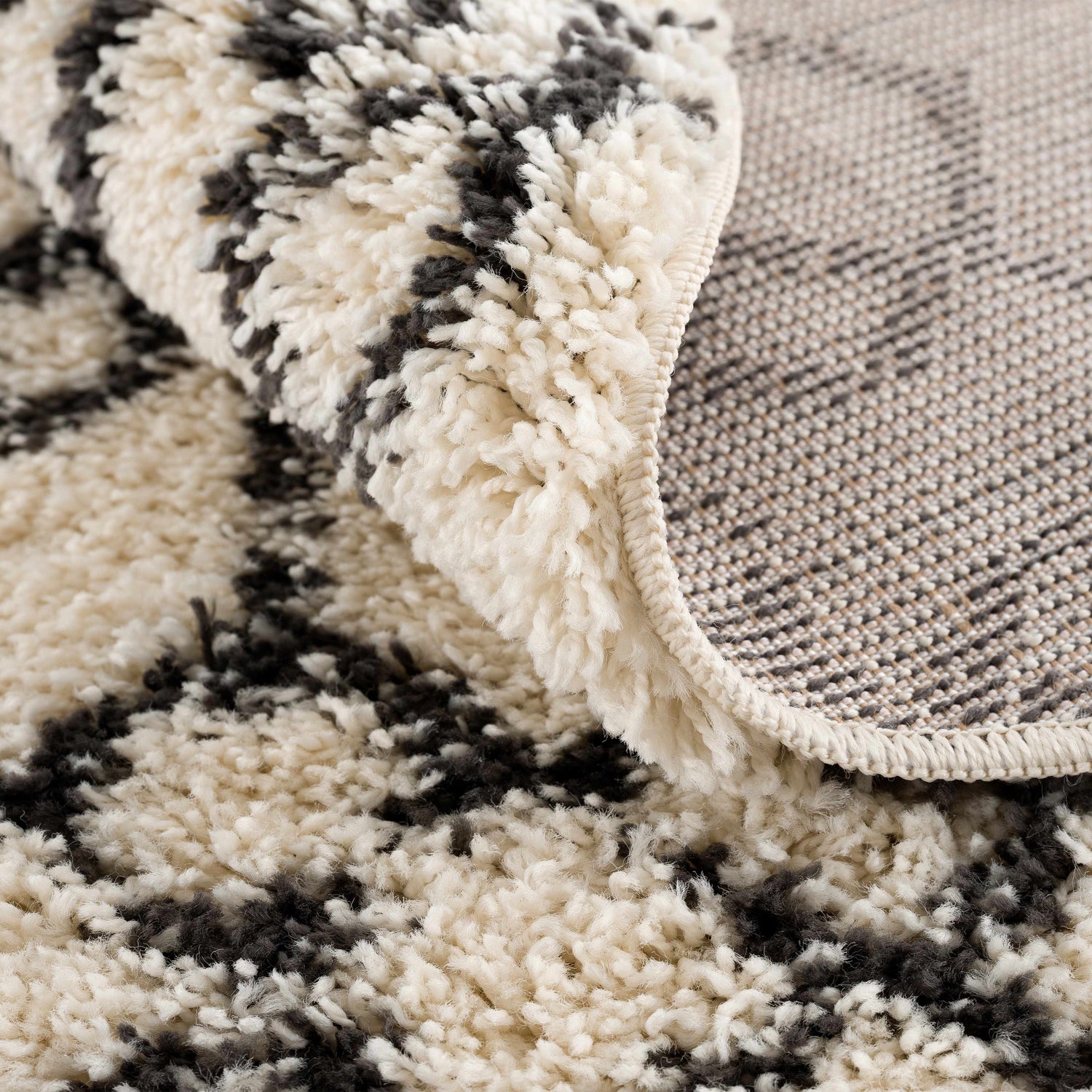 Close-up of the Muni Berber Shag Rug, showing its charcoal and light beige colors, shag texture, and woven backing. Fold