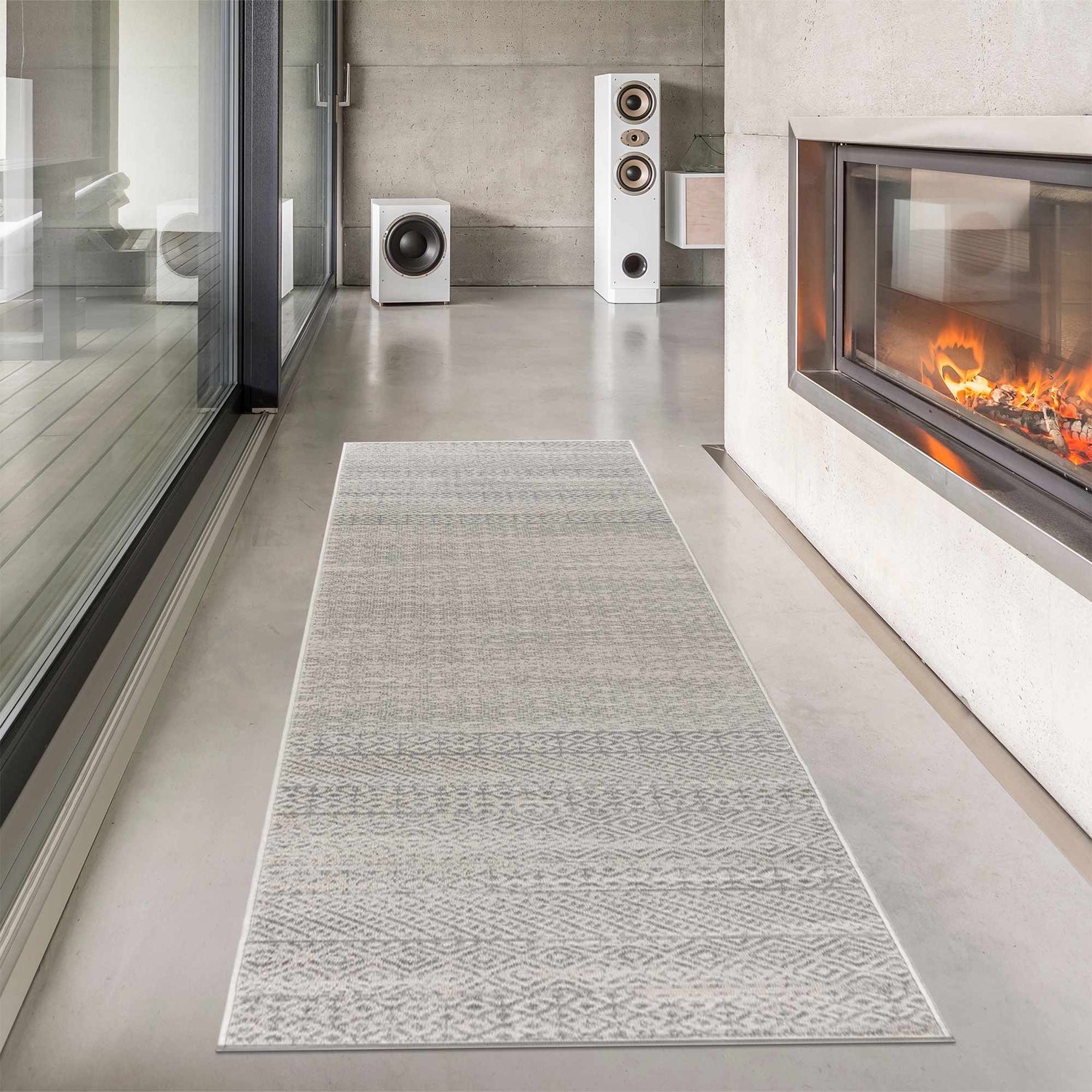Modern living room with Tigri Aztec Ivory & Gray rug runner, fireplace, and speakers. Concrete walls and floors. Roomscene-Runner