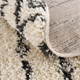 Close-up of Bayanga area rug showing the shag texture, charcoal Aztec pattern, and durable polypropylene backing. Fold