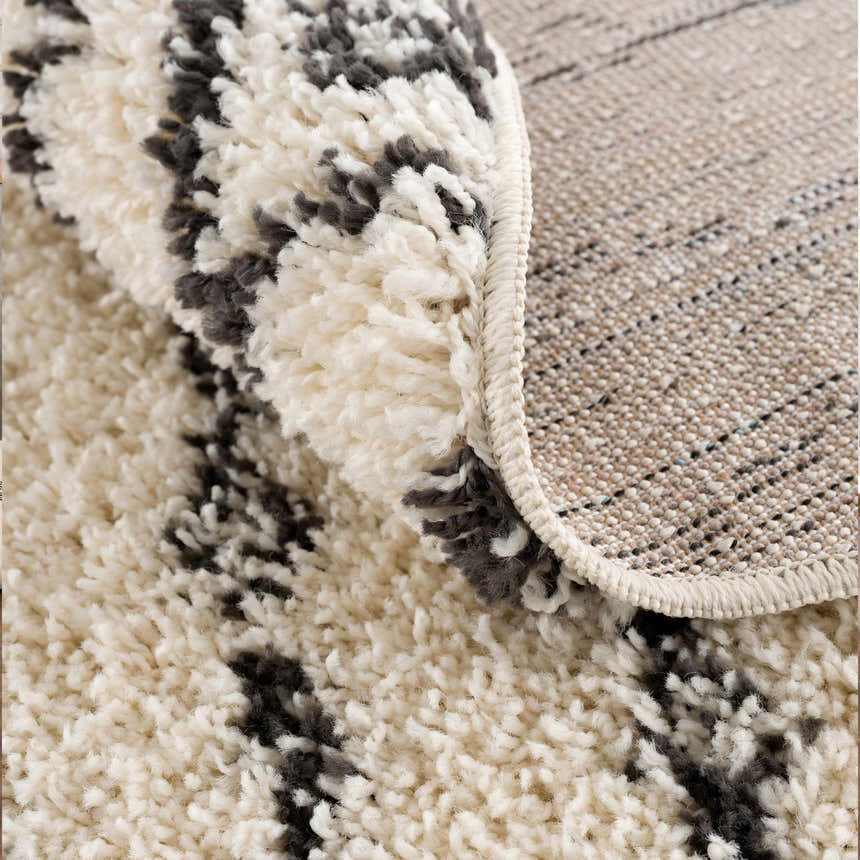 Close-up of Bayanga area rug showing the shag texture, charcoal Aztec pattern, and durable polypropylene backing. Fold