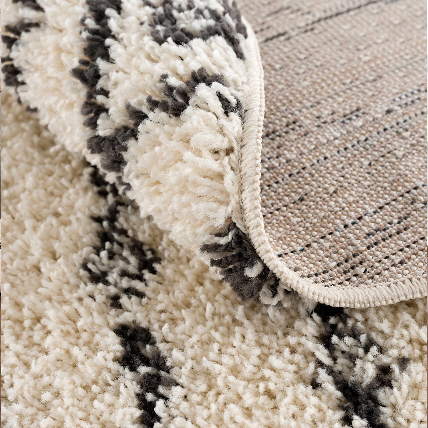 Close-up of Bayanga area rug showing the shag texture, charcoal Aztec pattern, and durable polypropylene backing. Fold