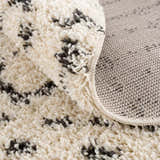 Close-up of the Kibureau Area Rug showing its beige shag texture and charcoal Moroccan-inspired pattern. Fold