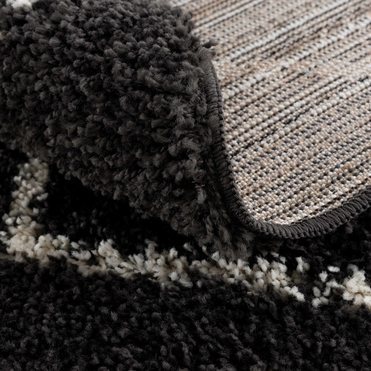 Close-up of the charcoal and light beige Ennis Area Rug showing shag texture and backing. Fold