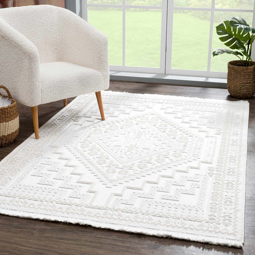 Living room scene with Ivory Alya 3D Medallion Fringe Area Rug, white chair, wood floors, and natural light. Roomscene-Rectangle