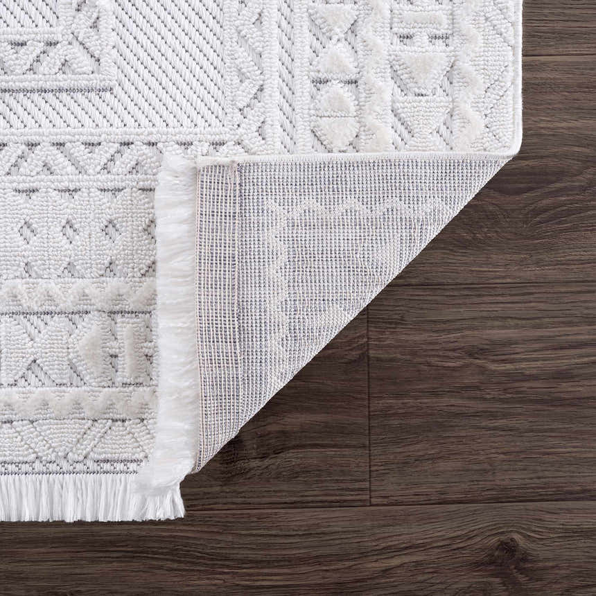 Close-up of Ivory Alya 3D Medallion Fringe Area Rug showing texture, fringe detail and backing on dark wood floor. Fold