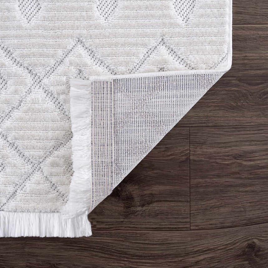 Close up of Ivory Beil 3D Fringe Area Rug showing geometric design, fringe detail, and rug backing on dark wood floor. Fold
