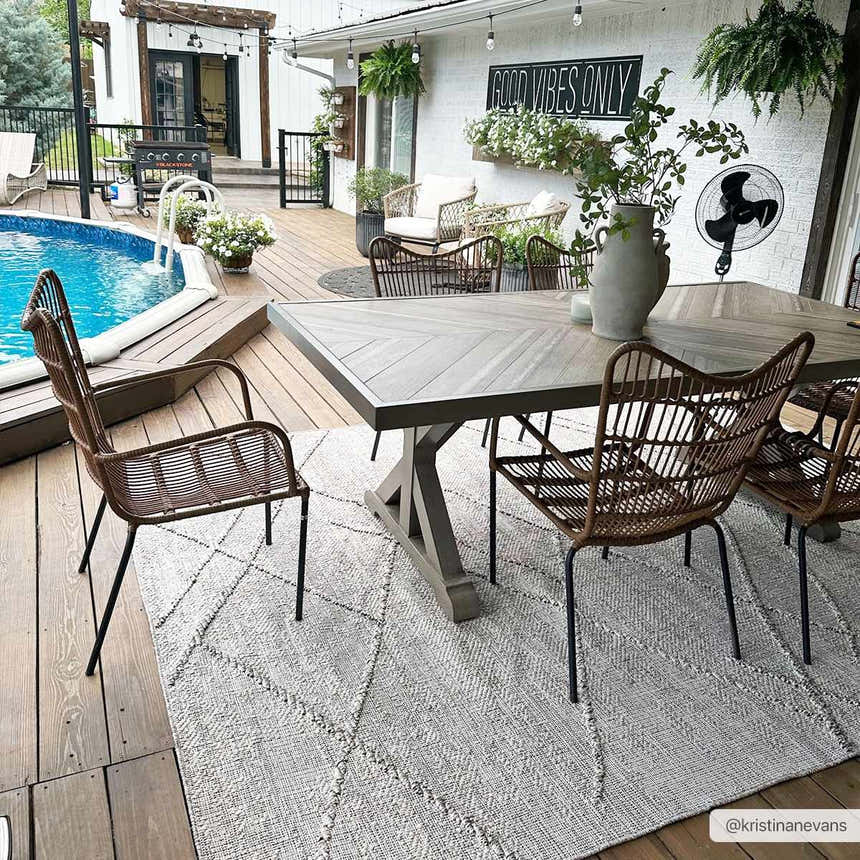 Outdoor dining area with Baqer Bone & Tan rug under a wood table and wicker chairs, poolside patio. Roomscene-Rectangle