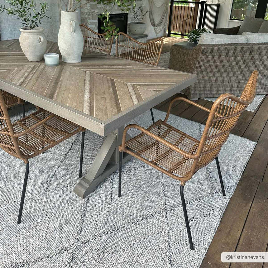 Outdoor dining area with a Baqer Bone & Tan Textured Performance Rug, wood table, and wicker chairs. Roomscene-Rectangle