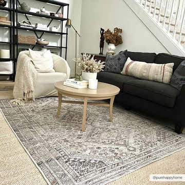 Living room scene with a Barny Beige Flat Pile Washable Rug, black sofa, beige armchair, and round coffee table. Roomscene-Rectangle