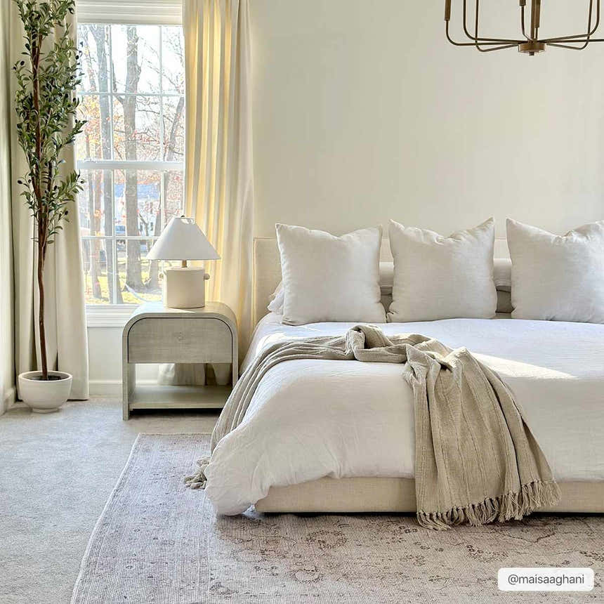 Neutral bedroom scene with a beige Bethany Vintage Flat Pile Washable Rug under a bed with white linens. Roomscene-Rectangle