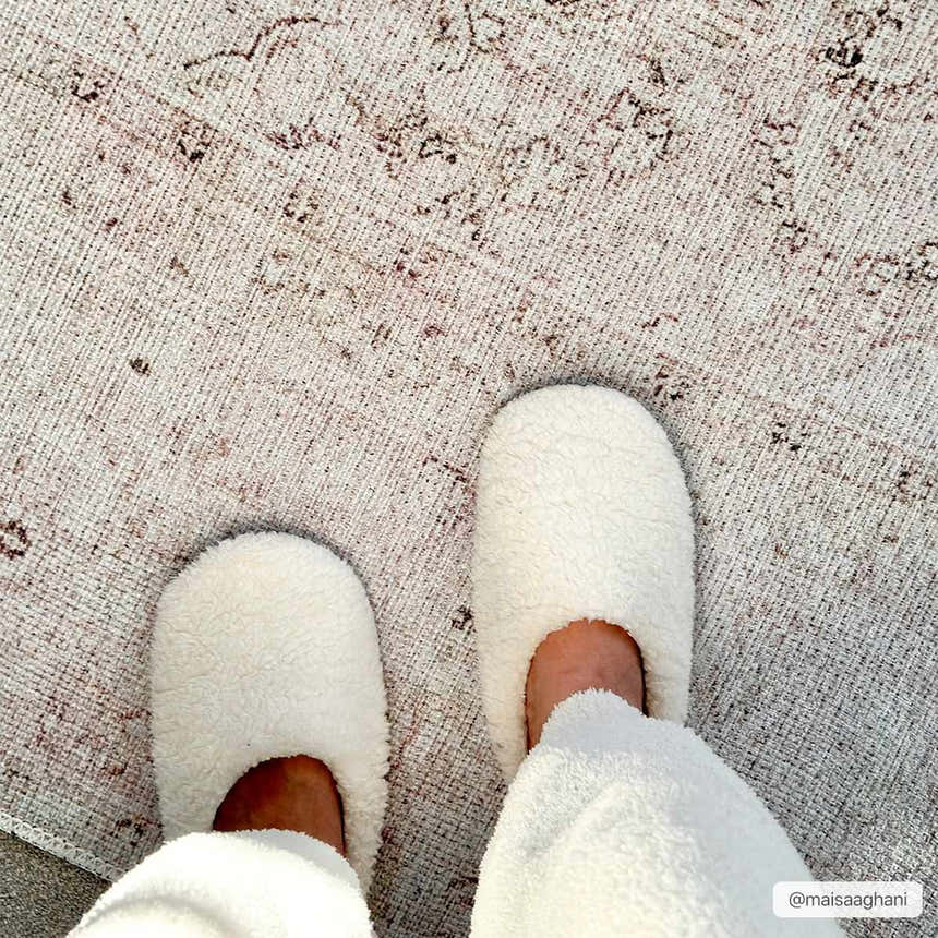 Close-up of a Bethany Vintage Flat Pile Washable Rug with beige, blush, and brown tones, paired with cozy white slippers. Styleshot