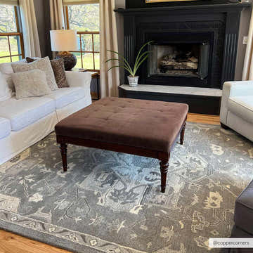 Living room scene with a taupe Broomfield 1196 wool rug under a brown ottoman, white sofa, and black fireplace. Roomscene-Rectangle