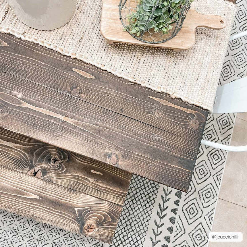 Close-up of the Burdette Soft Neutral Rug with charcoal, gray, and beige geometric patterns under a wooden table. Styleshot
