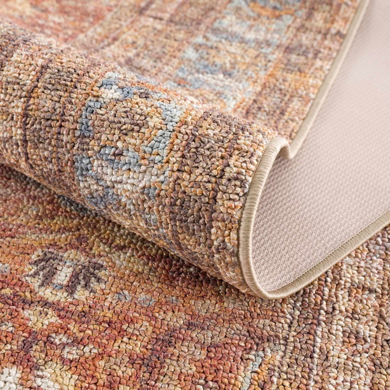 Close-up of the Anshu Peach Washable Area Rug showing its traditional vintage design, beige, blue, and burgundy colors, and soft texture. Fold