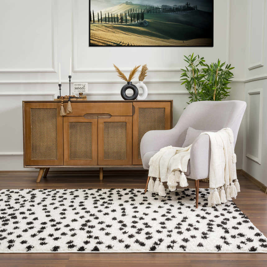 Living room scene with a Cansu Black & White Dotted Area Rug, a wooden sideboard, and a gray armchair with a throw. Roomscene-Rectangle