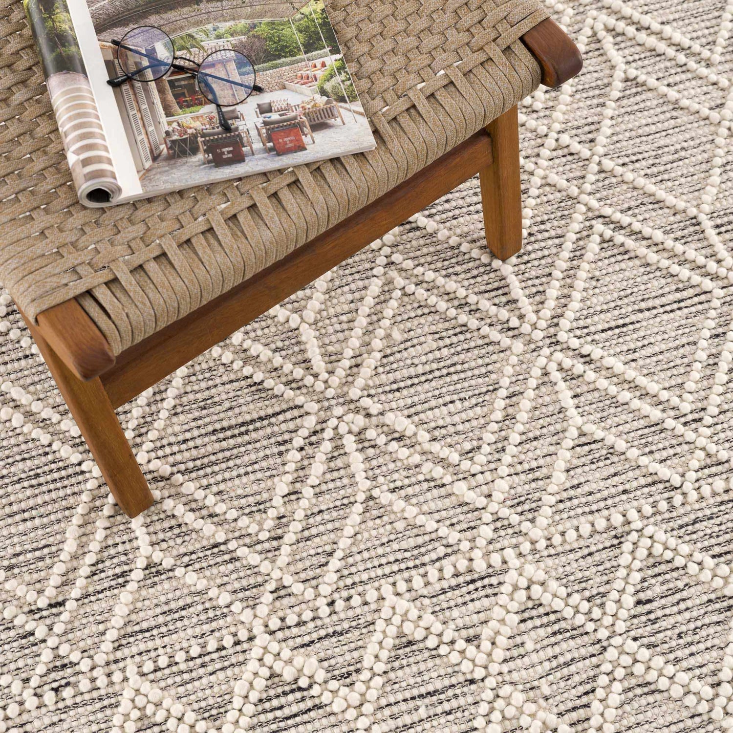 Close-up of the Ramsbury Wool Area Rug showing its black and ivory geometric pattern and hand-woven texture next to a chair. Styleshot
