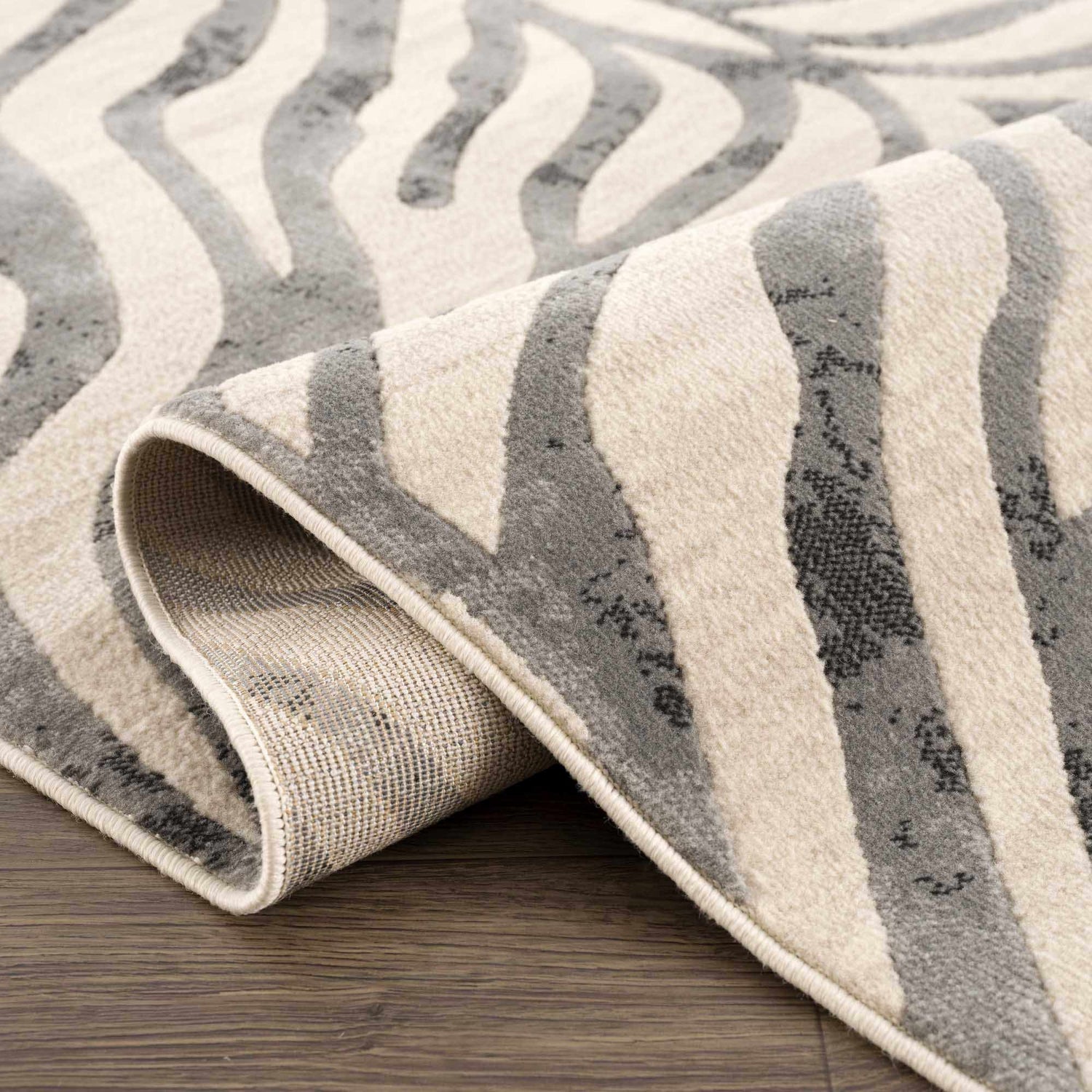 Close-up of the Gray Ecorse Zebra Print Area Rug, showing its gray, charcoal, and light beige animal pattern. Fold