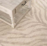 Close-up of a Beige Manteca Zebra Print Area Rug with a light wood coffee table. The rug has light beige and gray tones. Styleshot