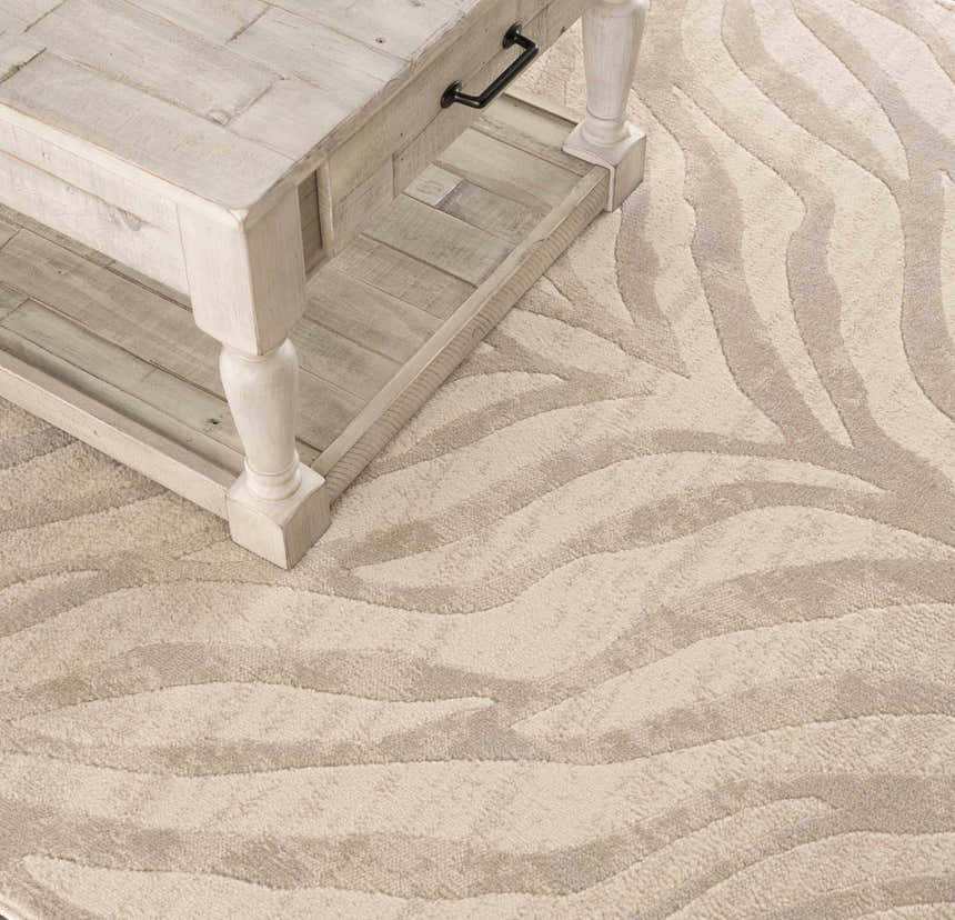 Close-up of a Beige Manteca Zebra Print Area Rug with a light wood coffee table. The rug has light beige and gray tones. Styleshot
