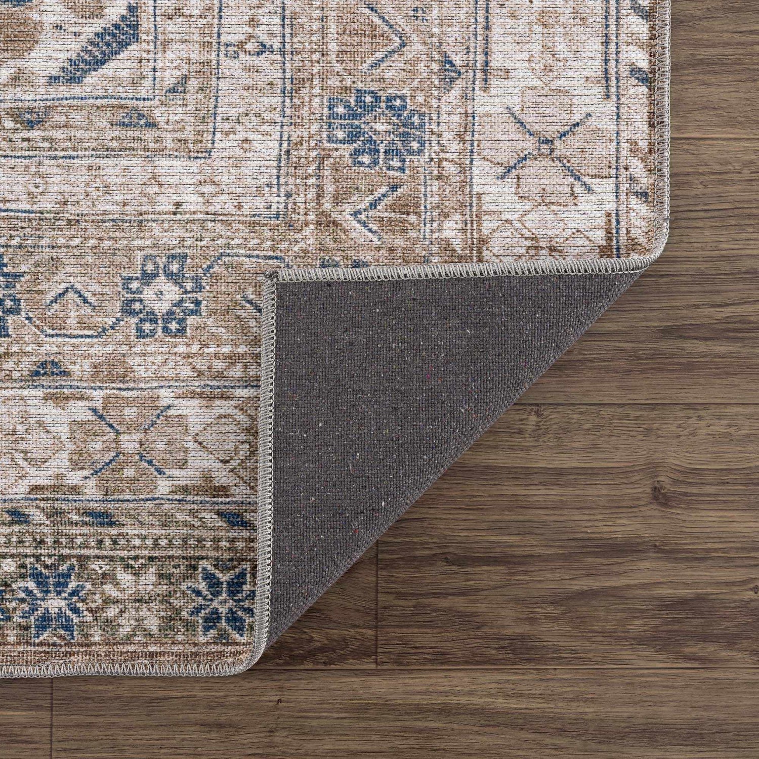 Close-up of the Baltinglass Flat Pile Washable Rug. Features a traditional pattern in blue, cream, and beige on a wood floor. Fold