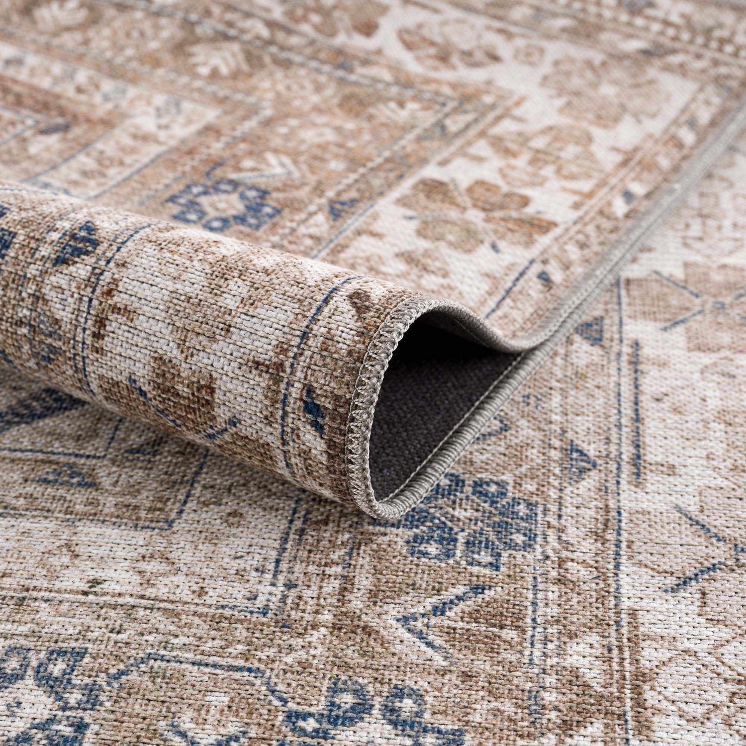 Close-up of the Baltinglass Flat Pile Washable Rug. Features a traditional pattern in blue, cream, and beige tones. Machine woven texture. Fold