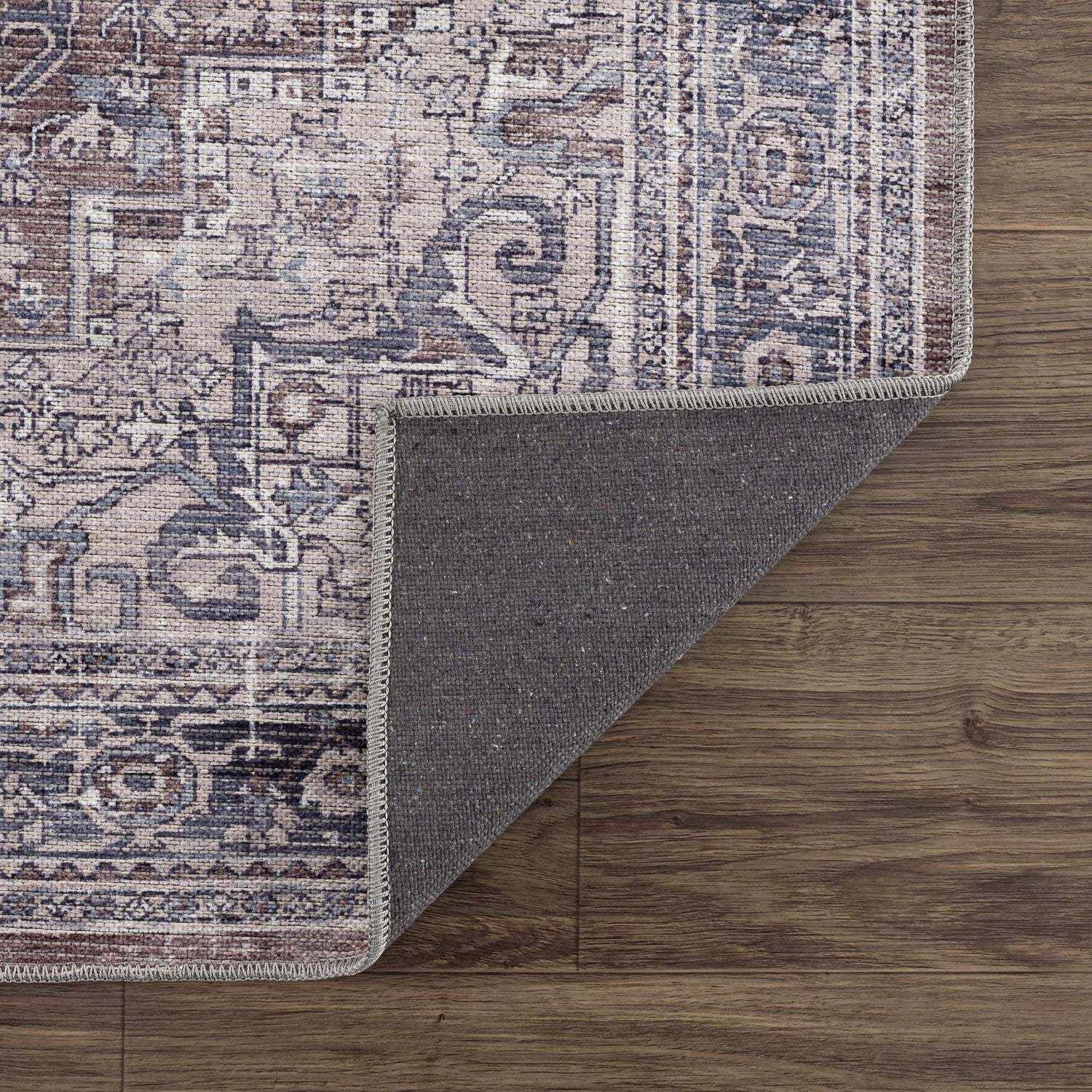 Close-up of the Abner Washable Area Rug showing its brown, denim, and ivory traditional pattern and gray backing. Fold