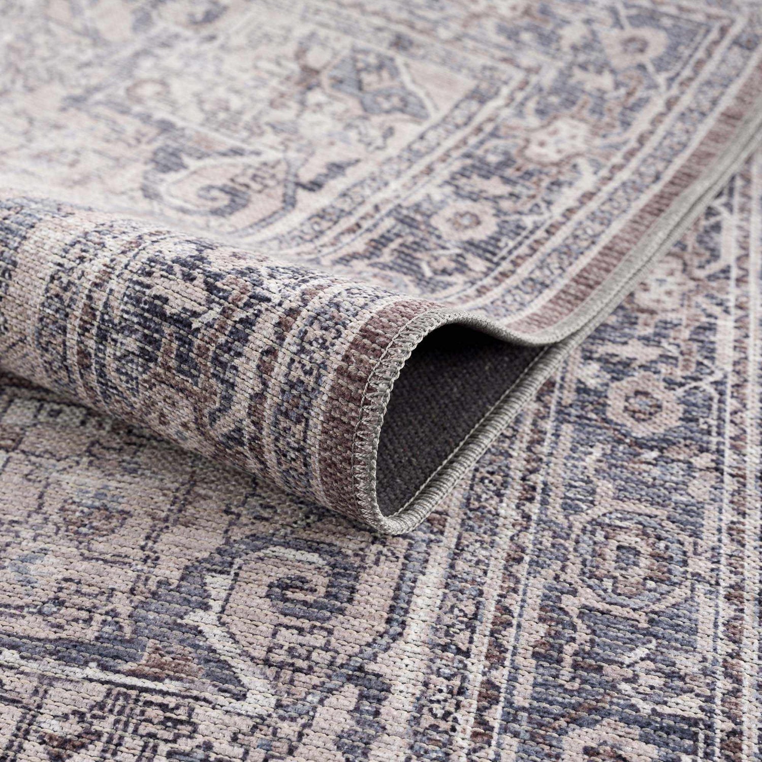 Close-up of the Abner Washable Area Rug, showcasing its traditional pattern, and colors in brown, charcoal, and light beige. Fold