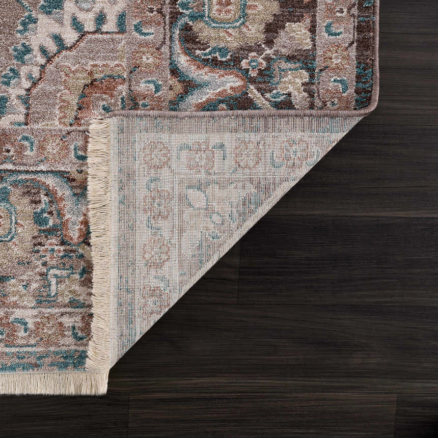 Close-up of the Baychester Brown Area Rug showing its traditional, oriental pattern, fringe, and dark brown, denim, and sage colors. Fold