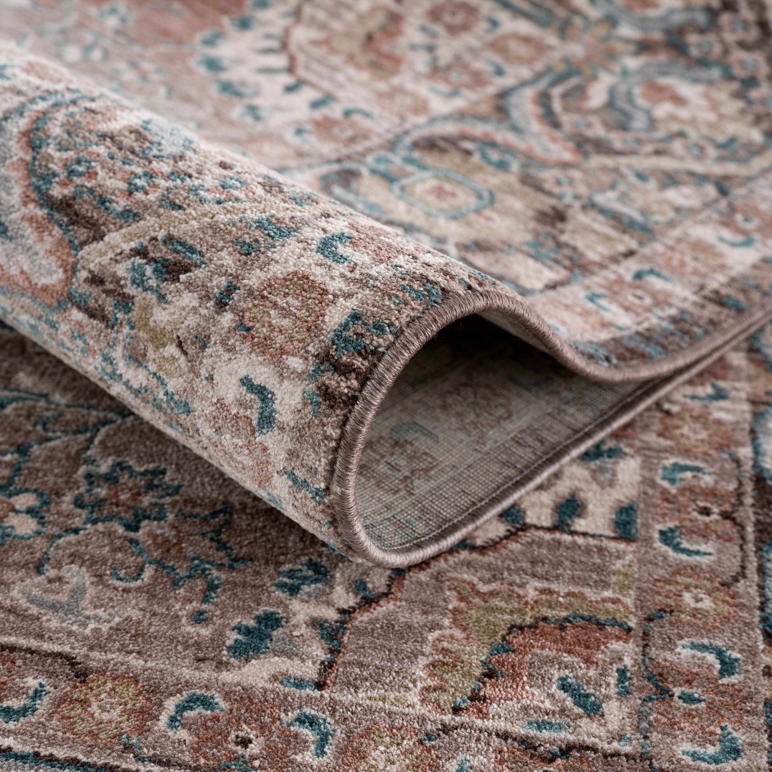 Close-up of the rolled-up Baychester Brown Area Rug, showing its traditional pattern, brown, pink, and teal colors. Fold