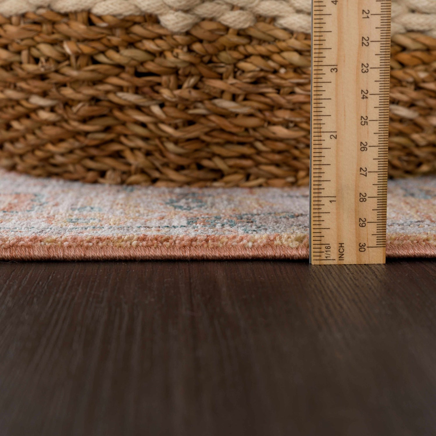 Close up of Cayla Area Rug showing bone, clay, and garnet colors, plus rug thickness with ruler. Pile