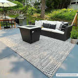 Outdoor patio scene with Cheverly Area Rug, black fire pit, and black wicker sofa with white cushions. Roomscene-Rectangle