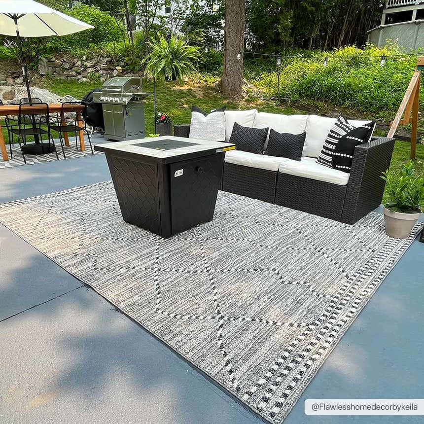 Outdoor patio scene with Cheverly Area Rug, black fire pit, and black wicker sofa with white cushions. Roomscene-Rectangle
