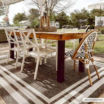 Outdoor dining area with a wood table and white chairs on a Coonamble Bordered Antrasit Rug. Roomscene-Rectangle