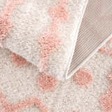 Close-up of Darva Pink Plush Area Carpet showing its soft, shag texture and bohemian pink diamond pattern. Fold