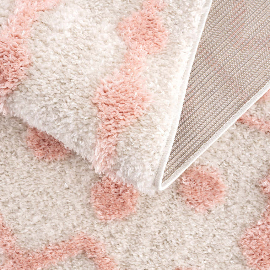 Close-up of Darva Pink Plush Area Carpet showing its soft, shag texture and bohemian pink diamond pattern. Fold
