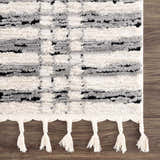 Close-up of the Nava Area Rug. Beige, black, and bone geometric pattern with tassels. Contemporary, Scandinavian style. Swatch