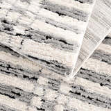 Close-up of the Nava Area Rug, showcasing beige, black, and bone geometric pattern and textured, machine-woven construction. Fold