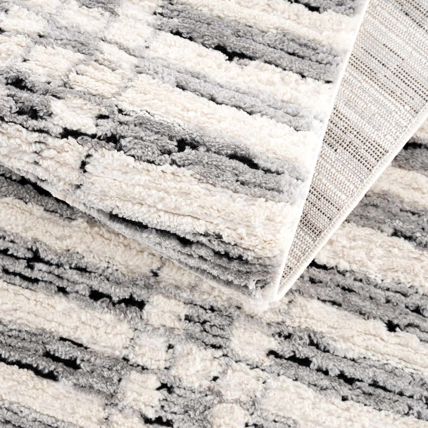 Close-up of the Nava Area Rug, showcasing beige, black, and bone geometric pattern and textured, machine-woven construction. Fold