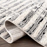 Close-up of the Nava Area Rug. Beige, black, and bone stripes with a textured, machine-woven pile. Geometric pattern. Fold