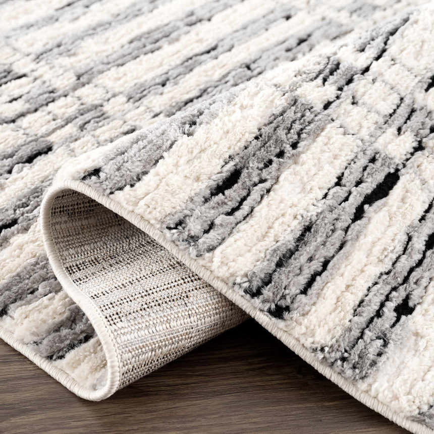 Close-up of the Nava Area Rug. Beige, black, and bone stripes with a textured, machine-woven pile. Geometric pattern. Fold