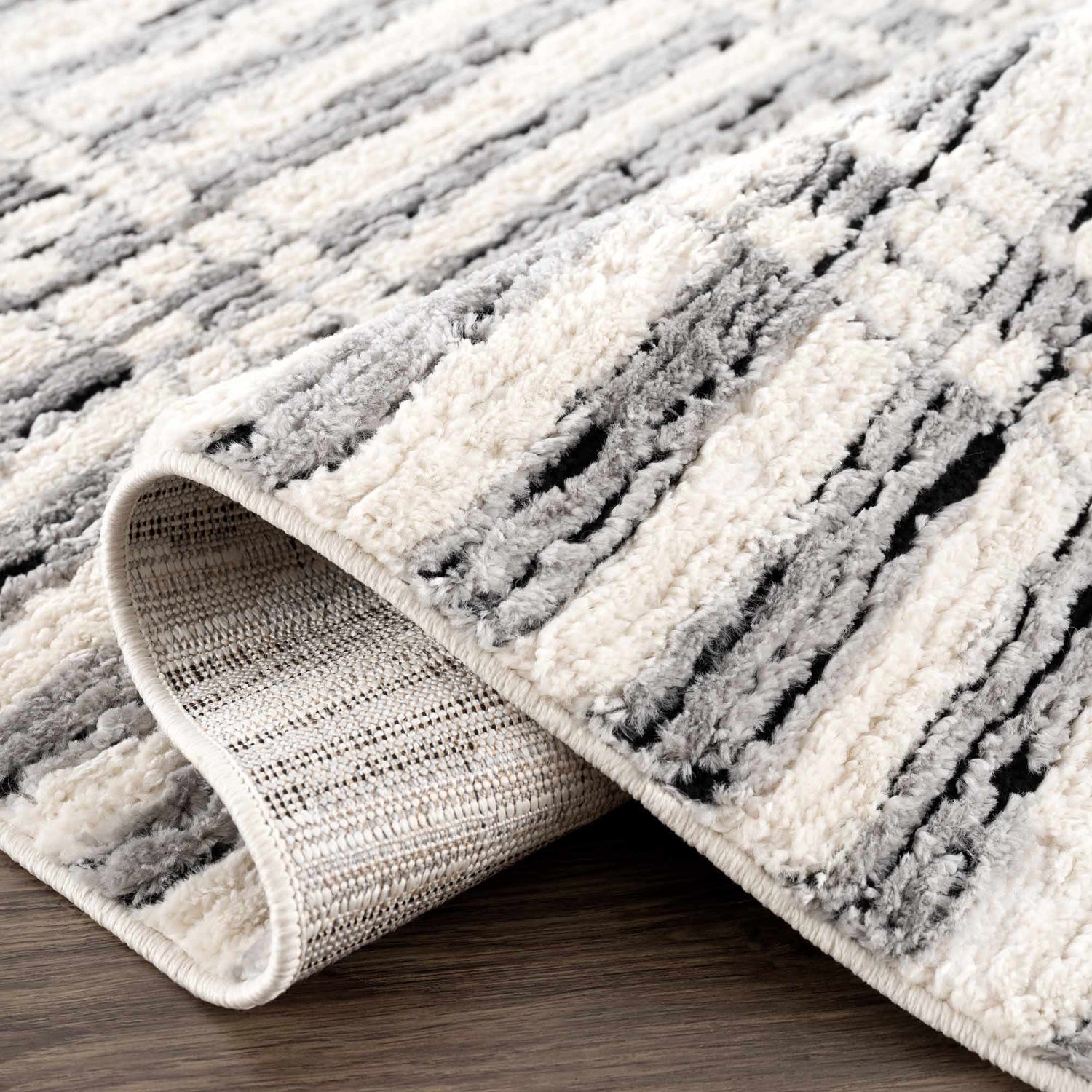 Close-up of the Nava Area Rug. Beige, black, and bone stripes with a textured, machine-woven pile. Geometric pattern. Fold